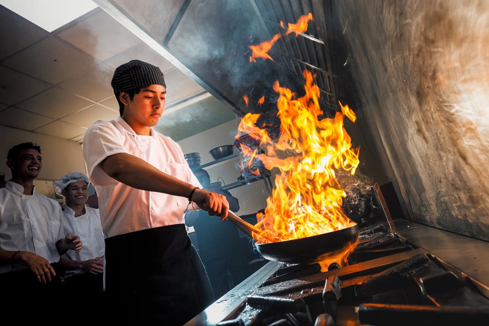 A cook in the restaurant kitchen making flambe in the frying pan