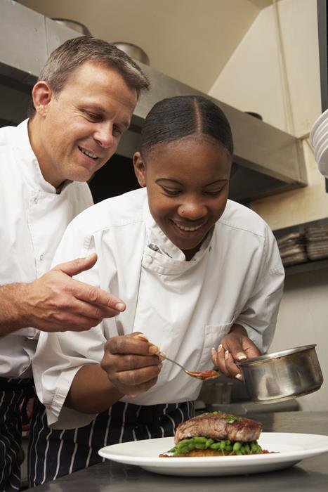 A mature male chef instructing a young female chef