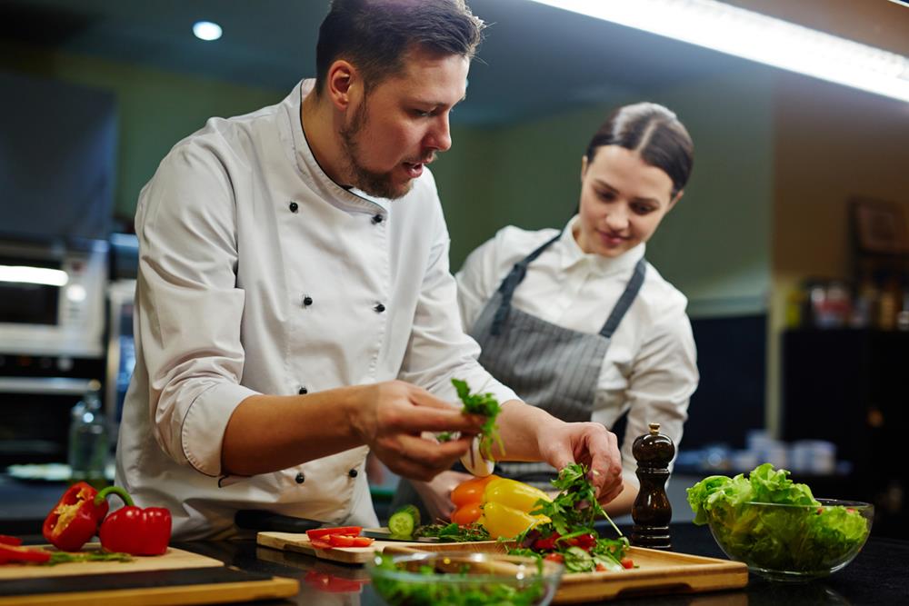 Chef consulting his trainee while preparing salad