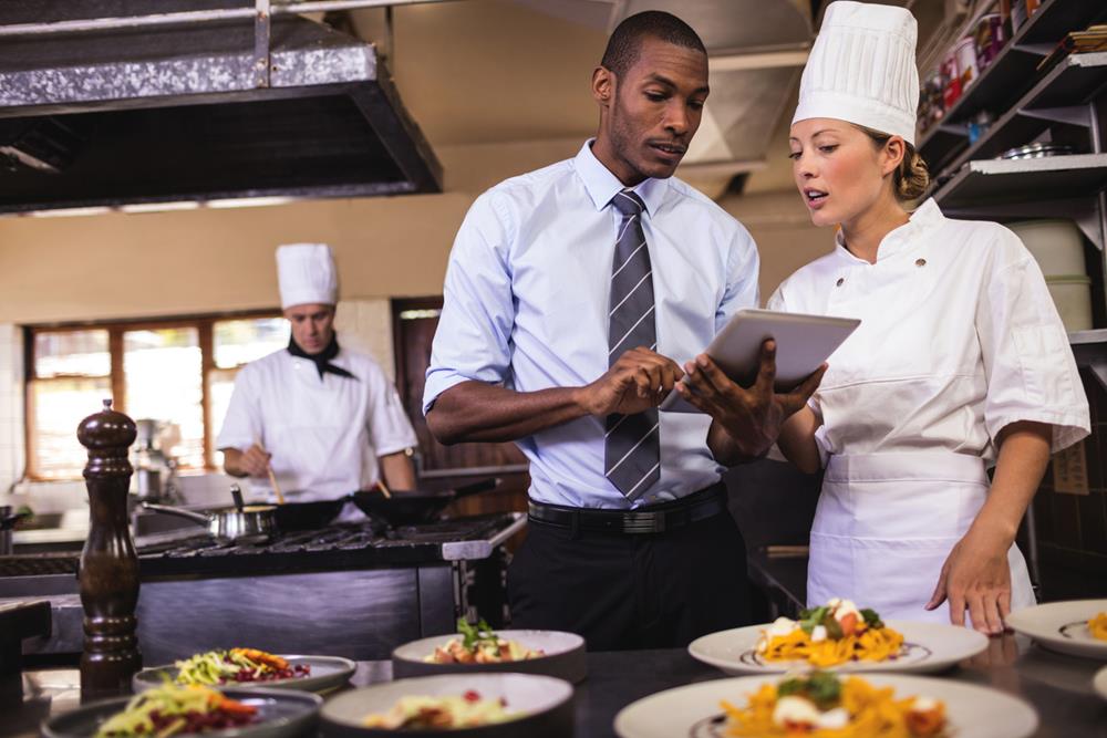 A manager and female chef using a tablet at the kitchen