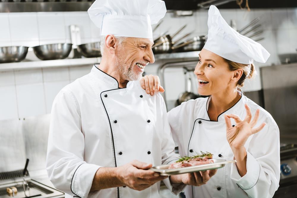 A mature male chef presenting a dish to a female sous chef showing OK sign