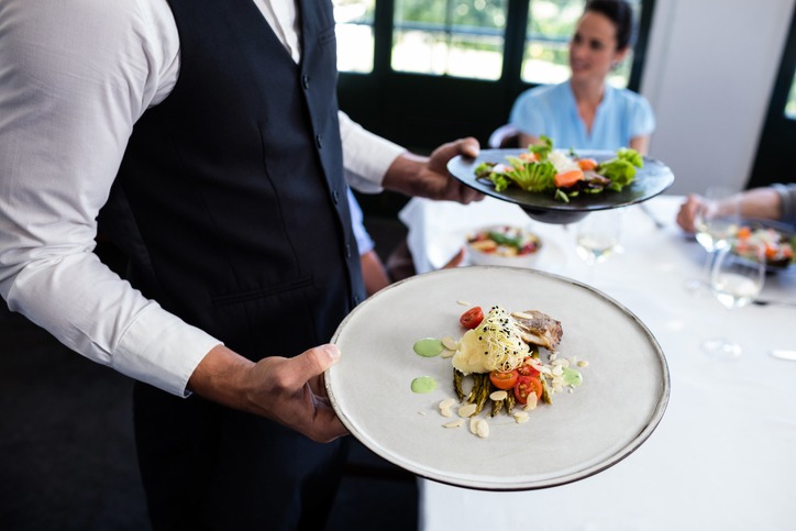 Portrait of a waiter standing with a meal next to customers