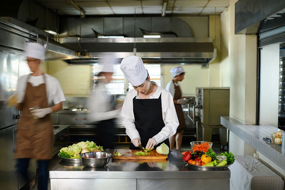 Chef apprentice working on vegetable preparation in a busy kitchen
