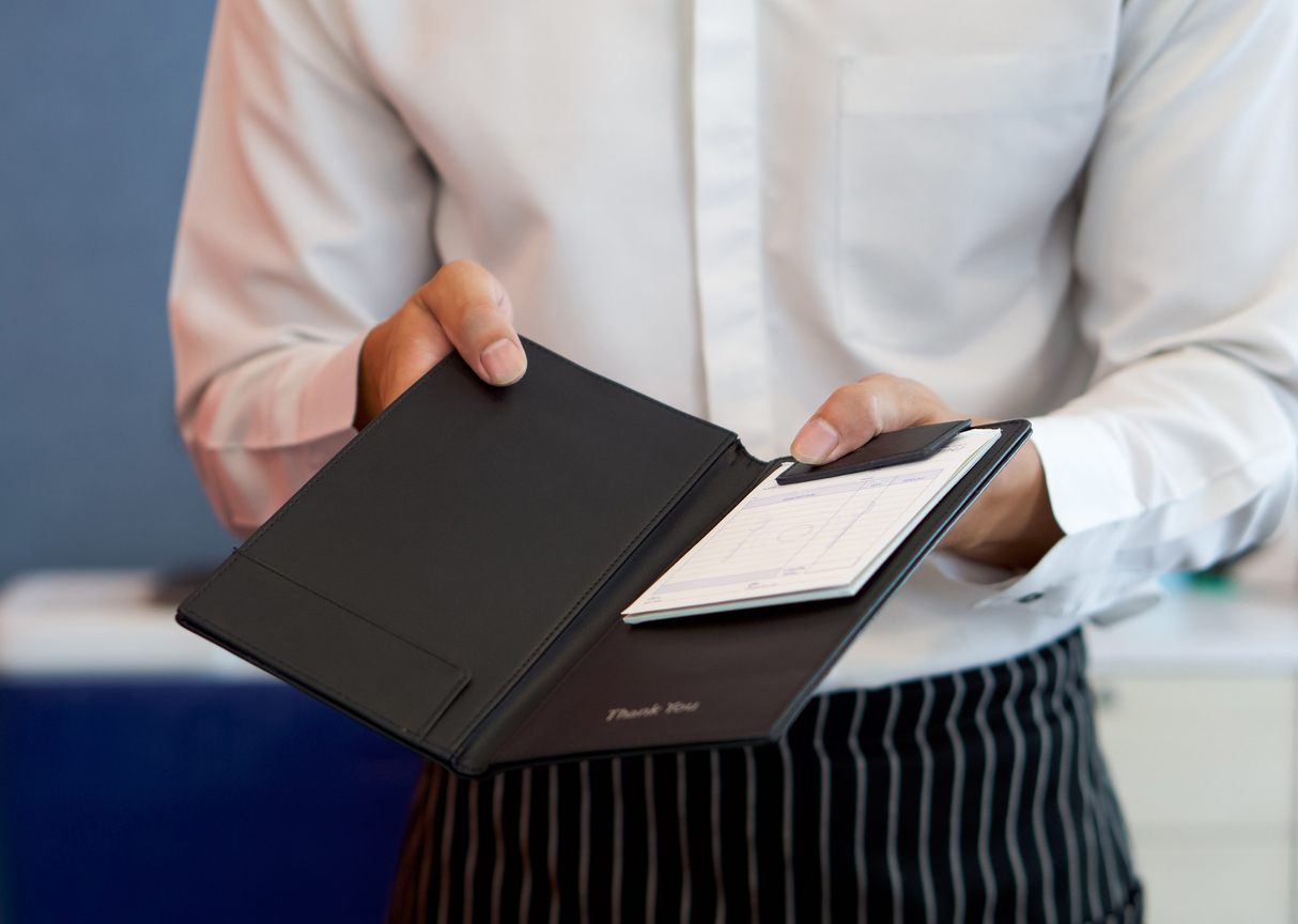The waiter in a white shirt and apron presents a receipt after calling the bill