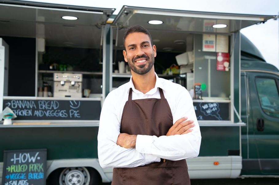 A waiter standing in front of a food truck and smiling