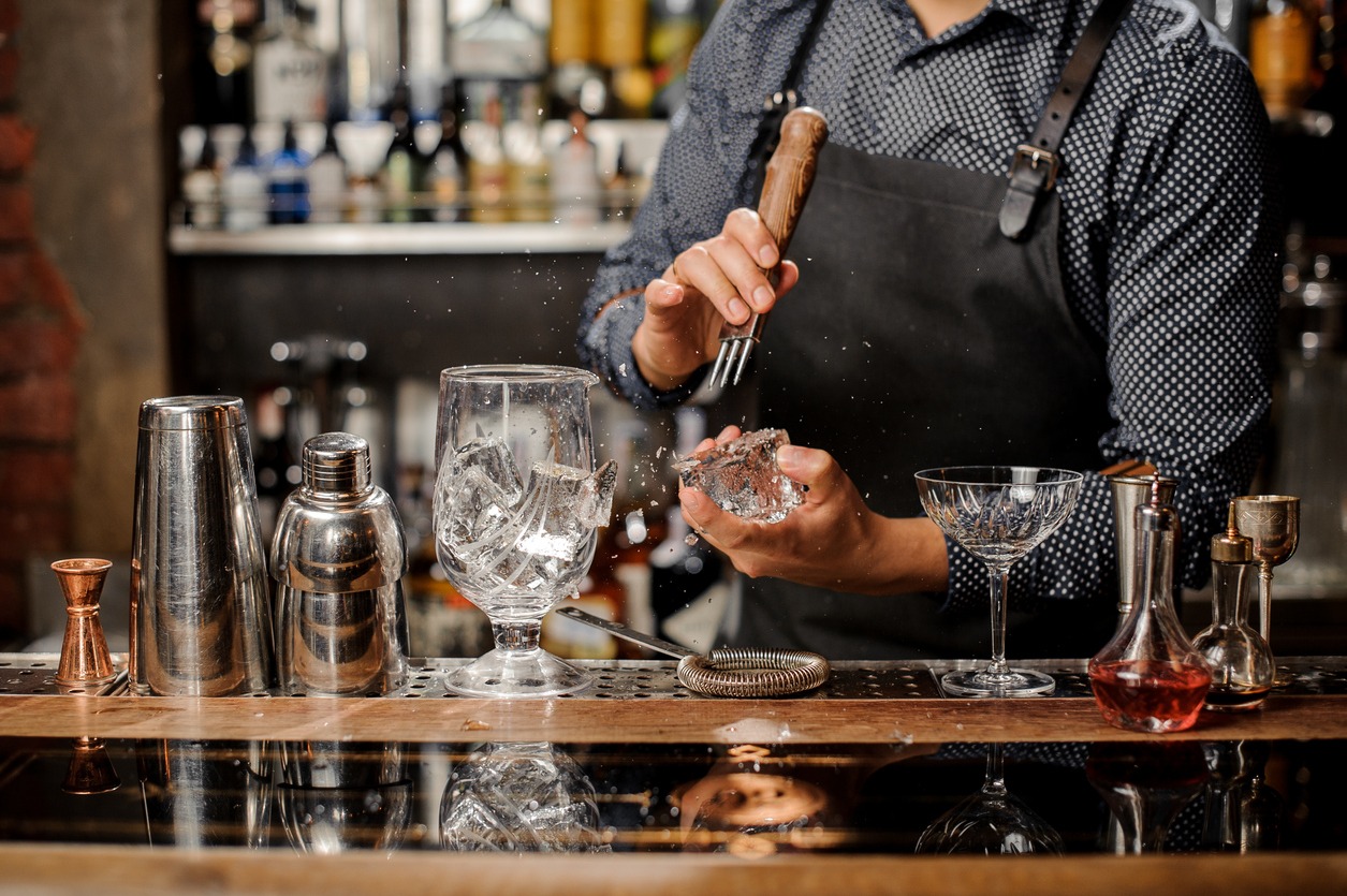 a barman crushing ice with a variety of bar tools lined up